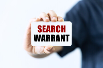 Search warrant text on blank business card being held by a woman's hand with blurred background. Business concept about search warrant.