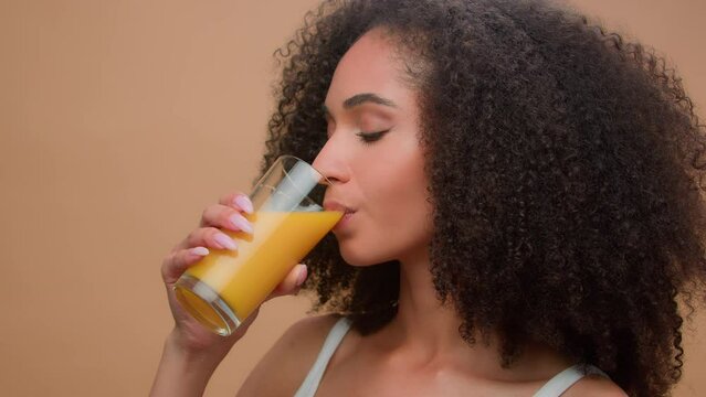 Beautiful happy healthy African American woman ethnic girl female model with curly hair drinking fresh orange juice vitamin drink diet detox organic vegetarian health care smiling in studio background