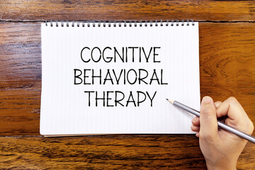Cognitive behavioral therapy handwriting text on blank notebook paper on wooden table with hand...
