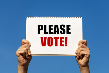 Please vote text on notebook paper held by 2 hands with isolated blue sky background. This message...
