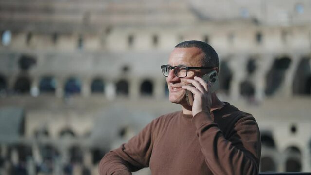 Cinematic shot of young man talking to phone at sightseeing of Colosseum, Rome. Slow motion cinematic shot with selective focus