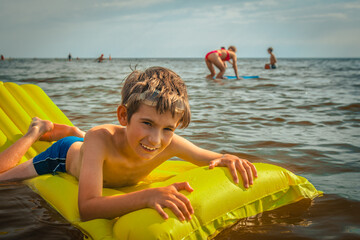 boy on an inflatable mattress in the sea. A smiling child is swimming in the sea with an inflatable mattress. Soft selective focus