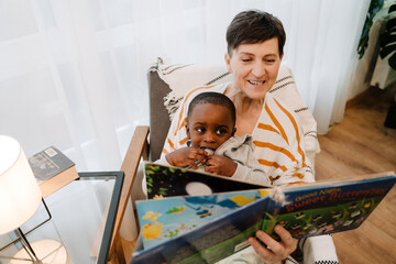 Mature woman sitting with her adopted son reading book