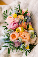 A detail shot of a gorgeous bridal bouquet with roses, peonies, yellow flowers in lots of springtime colors such as pink, yellow, coral orange, and pops of greenery.