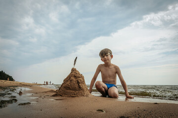 A boy made a pyramid out of sand on the seashore. A child was playing with sea sand on the sandy shore of the sea. Soft selective focus