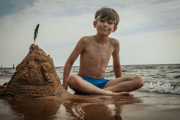 A boy made a pyramid out of sand on the seashore. A child was playing with sea sand on the sandy shore of the sea. Soft selective focus