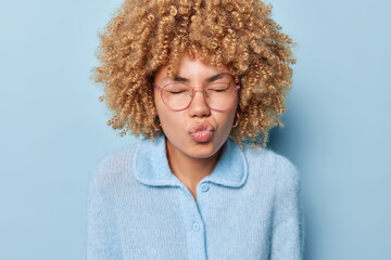 Indoor portrait of African girl wearing blue warm wool blouse with brown curly short hair rounded...