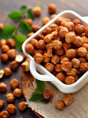 Peeled hazelnuts in white porcelain plate stand on table on wooden plank with burlap. Advertising photo of nuts. Top view. Background.