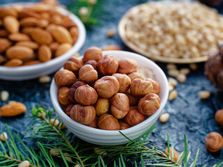 Nut assortment. Hazelnuts, almonds, pine nuts in plates stand on table with spruce branches. Top...
