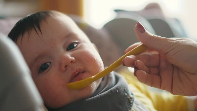 Healthy food. Cute baby girl face. beautiful a baby eats lifestyle dirty. Healthy food family concept. mother feeds her daughter baby with a spoon, the child is dirty. newborn baby breakfast
