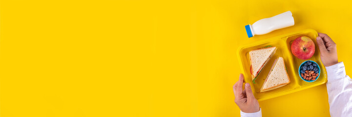 Healthy school meal, children packed lunch box with fruit, berry, nuts and sandwich with vegetables. Kids diet snack food with education school supplies, bright blue background top view copy space