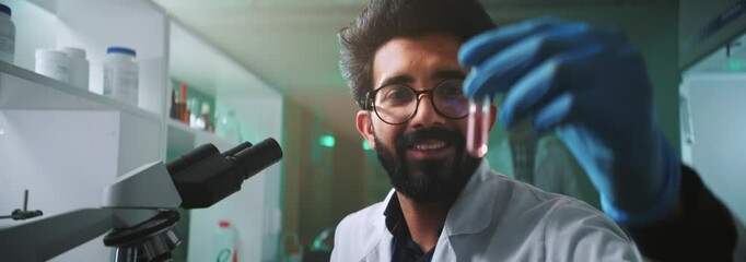 Happy young face man scientist with glasses and protective gloves holding a tube in a light laboratory. Medicine, biotechnology, chemistry