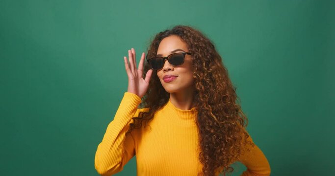 Beautiful young woman cool attitude tips sunglasses, flips hair, green studio
