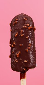 4K footage vertical video front view CU Time-lapse, Chocolate-covered almond popsicles melt on pink background.