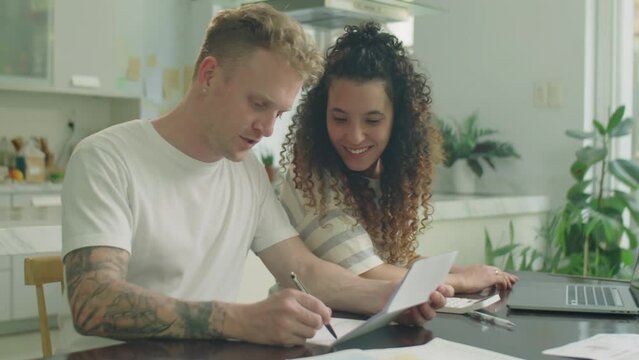 Medium shot of young couple discussing bills and using laptop while planning personal finance at home