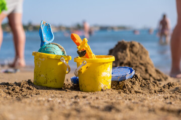 Children's beach toys - buckets, spade and shovel on sand on a sunny day. Bright toys on the background of the sea.