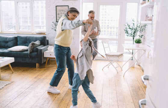 Cheerful grandparents teaching girl to dance in living room