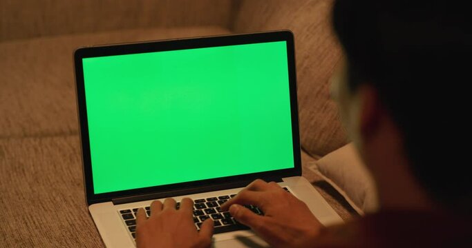 녹색 목업 화면이 떠 있는 노트북으로 일하는 남성을 어깨 너머에서 본 영상