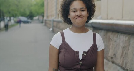 Portrait of delighted young African American lady laughing enjoying joke standing in city street looking at camera. People and happy youth concept.