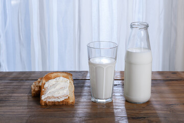 Glass of milk, bottle with milk and toast on a rustic wooden table in front of a window with a white curtain. breakfast