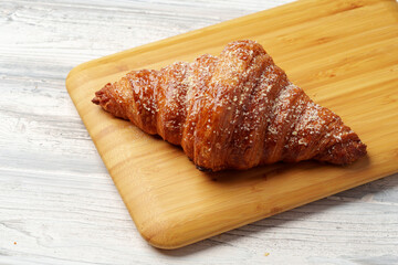 Freshly baked croissant with powdered sugar on wooden board