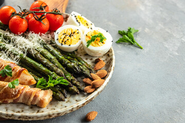 Fototapeta na wymiar Baked chicken breast wrapped in bacon with asparagus, eggs and tomatoes. Ketogenic diet. Low carb high fat breakfast. Healthy food concept. Long banner format. top view