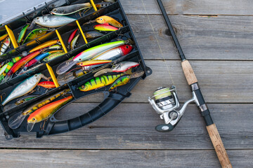 A fishing tackle box, complete with lures and fishing gear on a wooden background on top. A set of fishing lures for spinning fishing.