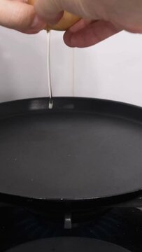A man's hands break an egg into a hot pan. Preparing breakfast. Vertical video