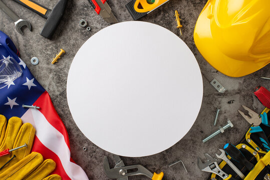Paying tribute to the hard work of construction workers on American Labor Day. Above shot of flag, helmet, gloves, and building tools on grunge textured grey concrete, empty circle for ads or text