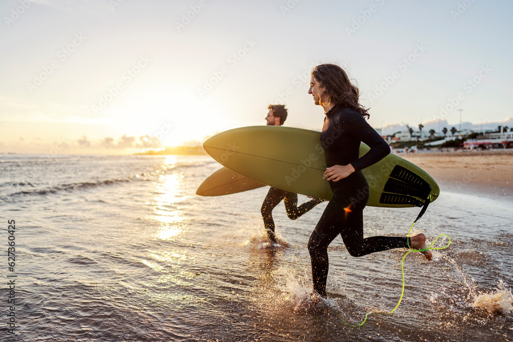 Wall mural Couple is running into the water with surfboards.