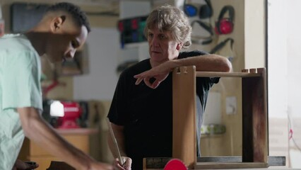 Carpenter orienting apprentice at woodworking carpentry workshop . Candid teacher talking with student