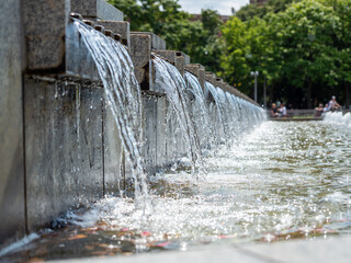 Water flows over the stone slabs of the city fountain. Fountain in the city park.