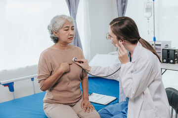 Asian doctor talking to old woman patient about symptoms of disease The doctor uses a stethoscope...