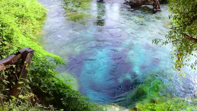 Unique karst source of water gushing from the ground called the Blue Eye or Syri i Kalter. Natural phenomenon occurring in the village of Muzine, Albania. River framed by green trees.