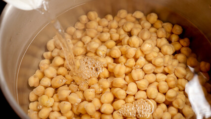 Slow motion of pouring boiling water in pan with cooking chickpeas. Cooking egume, healthy nutrition, vegan food.