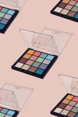 Pattern of eye shadow make up palette with bright vivid colours on a pink background with sunny shadow and copy space. Summer makeuo ideas of colorful eye powder shadow.