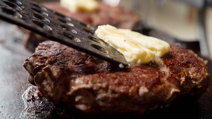 Macro shot of putting butter on hot burgers with spatula. Cooking at home, kitchen appliance, healthy nutrition, hamburger ingredients.