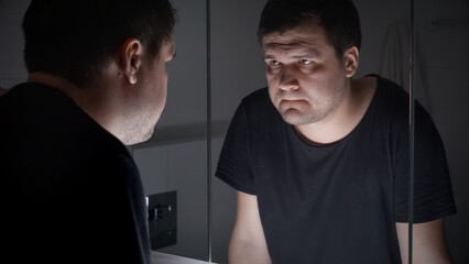 Upset and angry man in black t-shirt looking in his reflection at bathroom