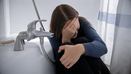 Upset crying woman sitting in bath after being victim of abuse or violence