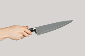 Closeup of woman hand holding huge sharp kitchen knife. Indoor studio shot isolated on gray...