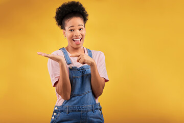Portrait, space and a black woman pointing to her palm for the promotion of a product on a yellow background in studio. Smile, advertising or marketing with a happy young female brand ambassador - obrazy, fototapety, plakaty