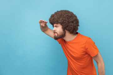 Side view of man with Afro hairstyle wearing orange T-shirt looking far away at distance with hand...