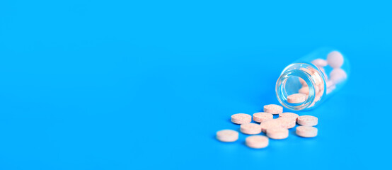 Pink pills are poured out of a glass bottle on a blue background. Vitamin B complex, copy space. Healthcare, medical pills and dietary supplements. Selective focus