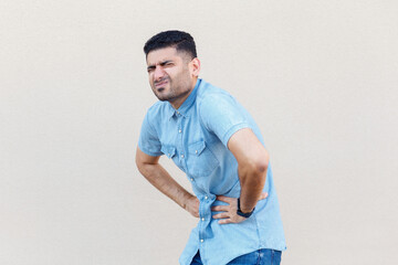 Portrait of sad sick unhealthy man wearing denim shirt frowning his face from terrible pain in his...