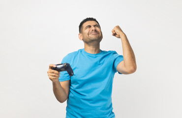 Cheerful unshaven man gamer wearing blue T- shirt standing playing video games, holding joystick...