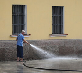 A man washes asphalt with a jet of water from a hose, Admiralteyskaya Embankment, Saint Petersburg, Russia, July 25, 2023