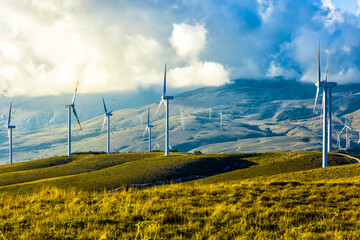 Industry conceptual photo for a clean environment. A wind farm with wind turbines among the great mountains, the clouds, the meadows and the grazing animals. Peace and quiet against pollution 
