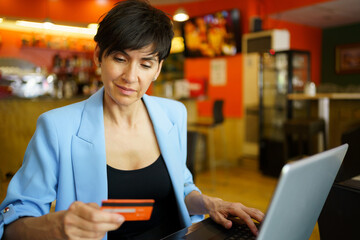 Middle age woman using laptop and debit card in cafe