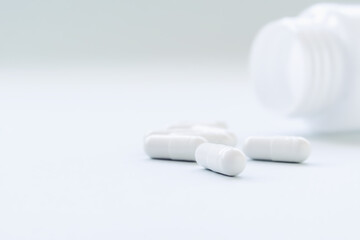 white pill capsules poured out of a white jar. medicines, treatment and medicine concept