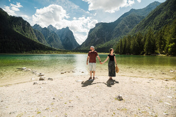 Fototapeta na wymiar Beautiful traveler couple in front of the iconic and stunning Lago di Dobbiaco, The Dolomites, Italy